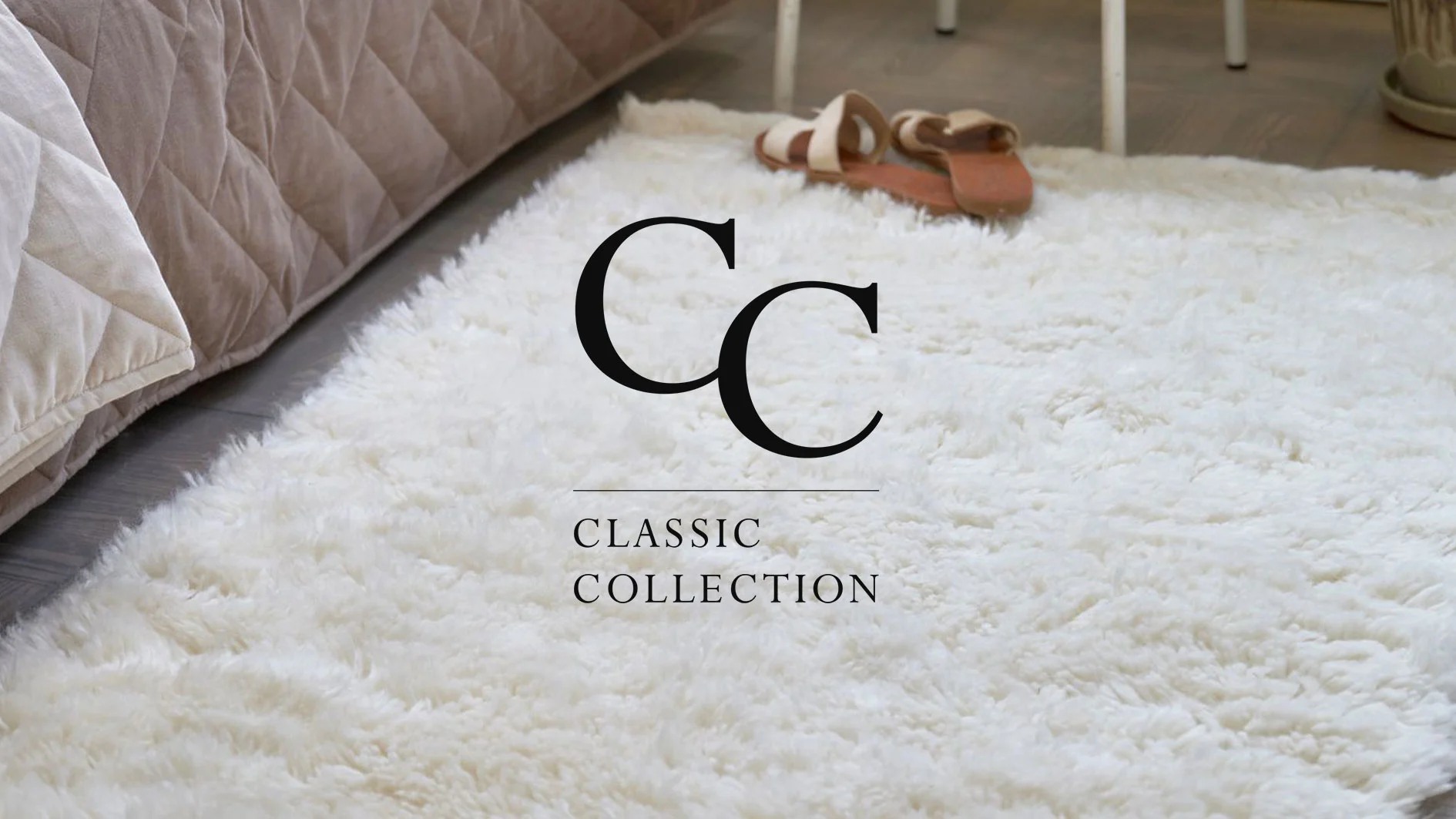 En fluffig vit matta på ett trägolv, med beige sängkläder och ett par sandaler i bakgrunden.