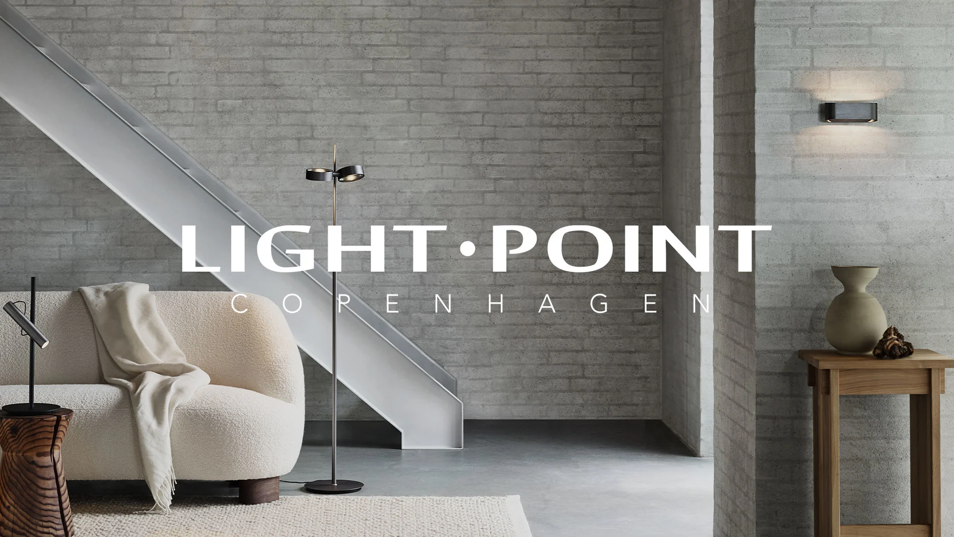 Modernt vardagsrum med betongväggar, vit soffa och modern belysning. Text: 'LIGHT POINT COPENHAGEN'.