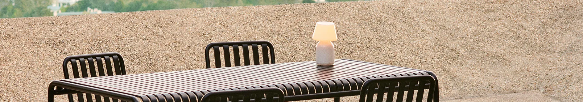 Mörkbrunt utomhusmatbord och stolar med ribbad skiva, med en liten lampa på bordet.
