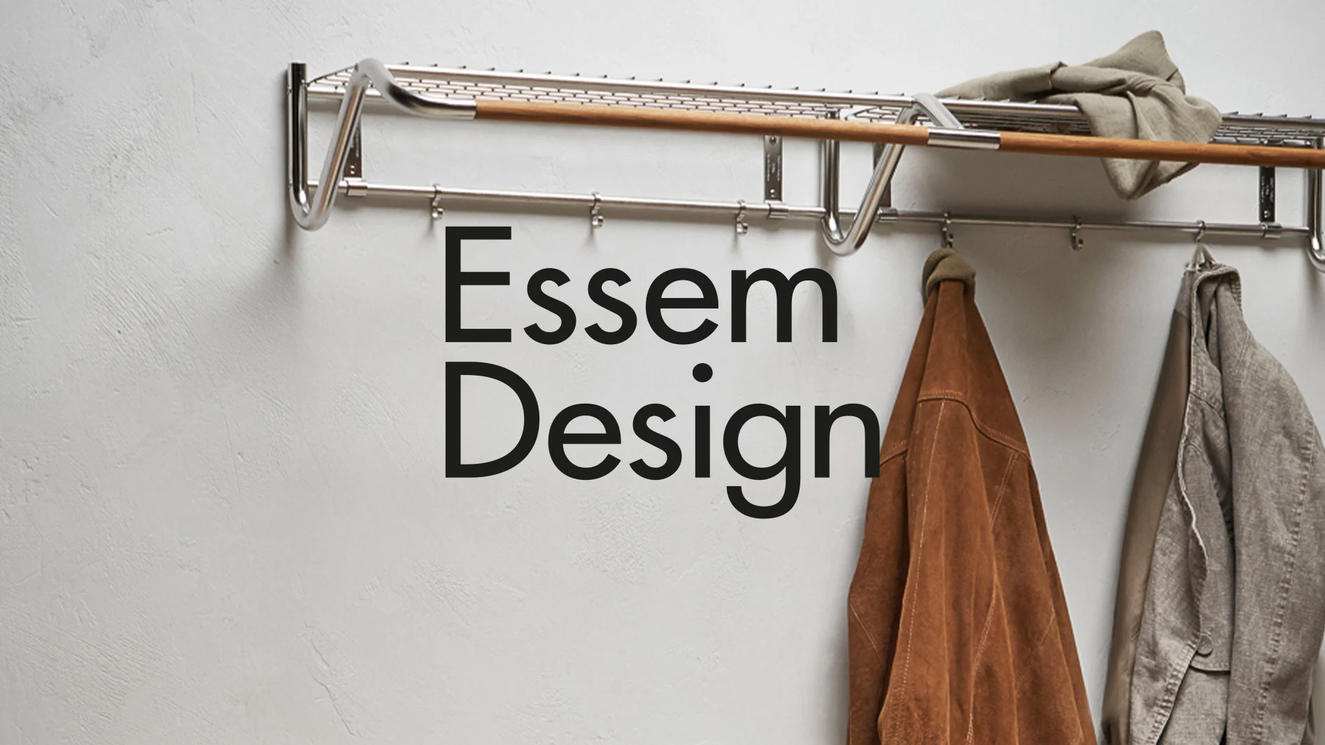 Klädhängare i metall och trä med en brun skinnjacka och en grå linnejacka, med texten «Essem Design».