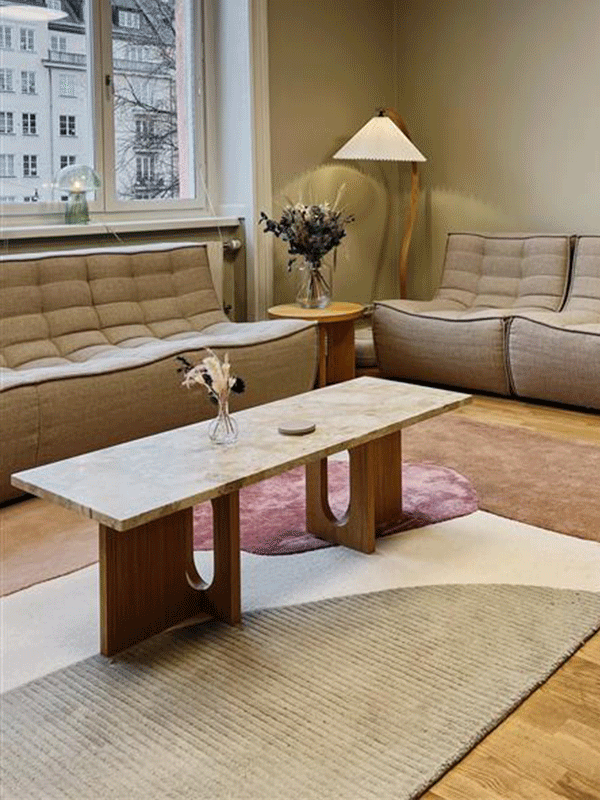 Ett modernt vardagsrum med ljusgrå soffa, beige matta, två mörkbruna bord och två olika lampor.