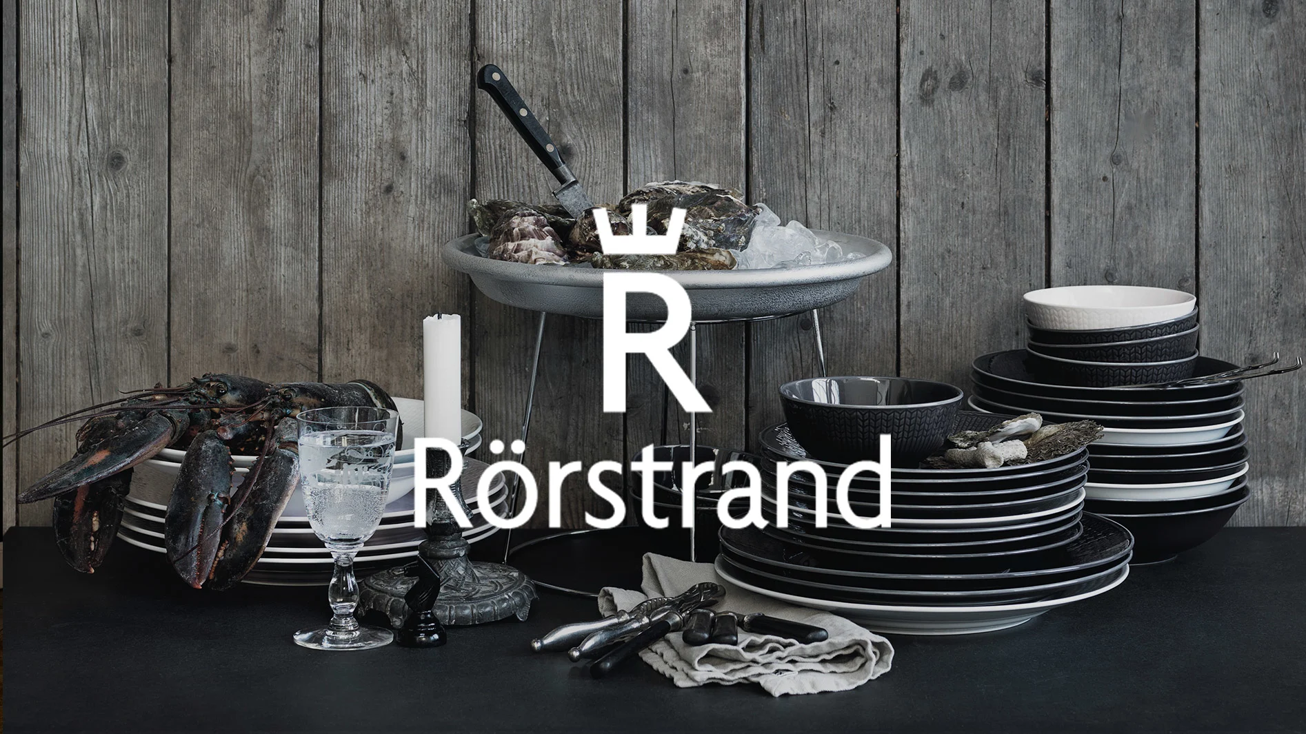 Rustik dukning med hummer, ostron på is, staplar med svart-vitt mönstrat porslin, med Rörstrand-logotypen.