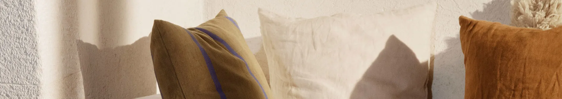 Tre kuddar: en olivfärgad med blå ränder, en ljusbeige och en roströd med en fluffig tofs.