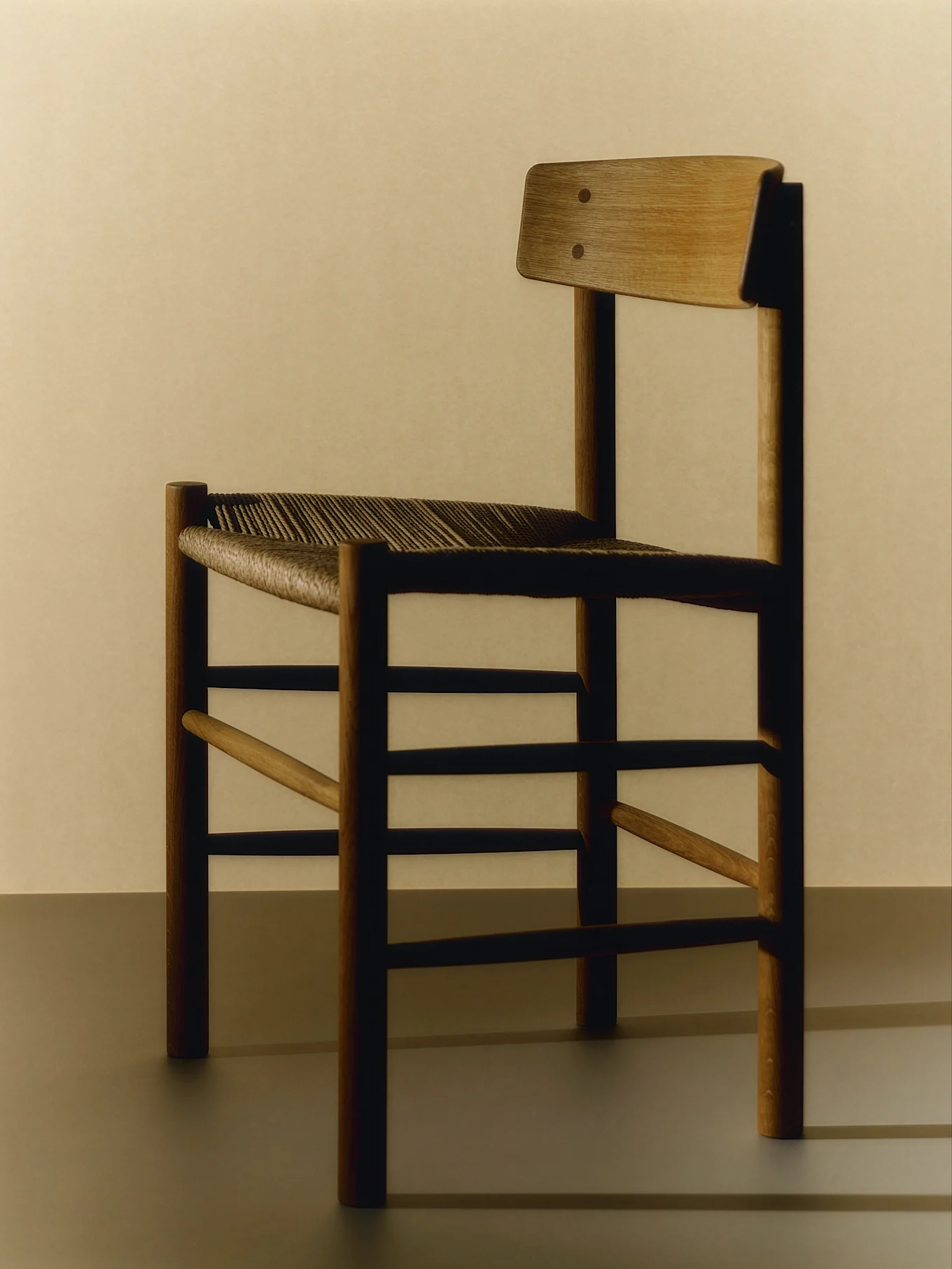 En minimalistisk trästol med flätad sits och ett rakt ryggstöd, sedd från sidan.