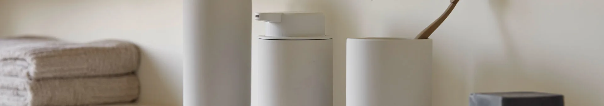 Beiga handdukar, vit tvålpump, vit mugg med en trätandborste, och en svart tvål.