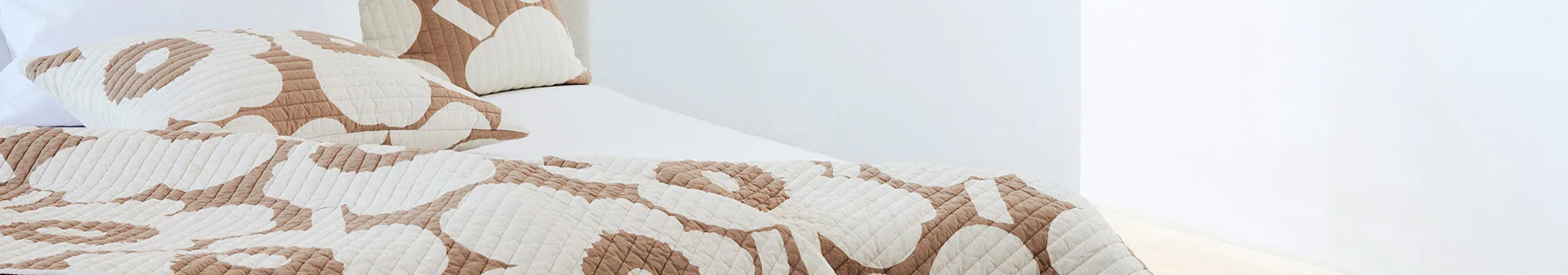 Quiltat överkast och kuddar i beige och off-white med ett abstrakt mönster.