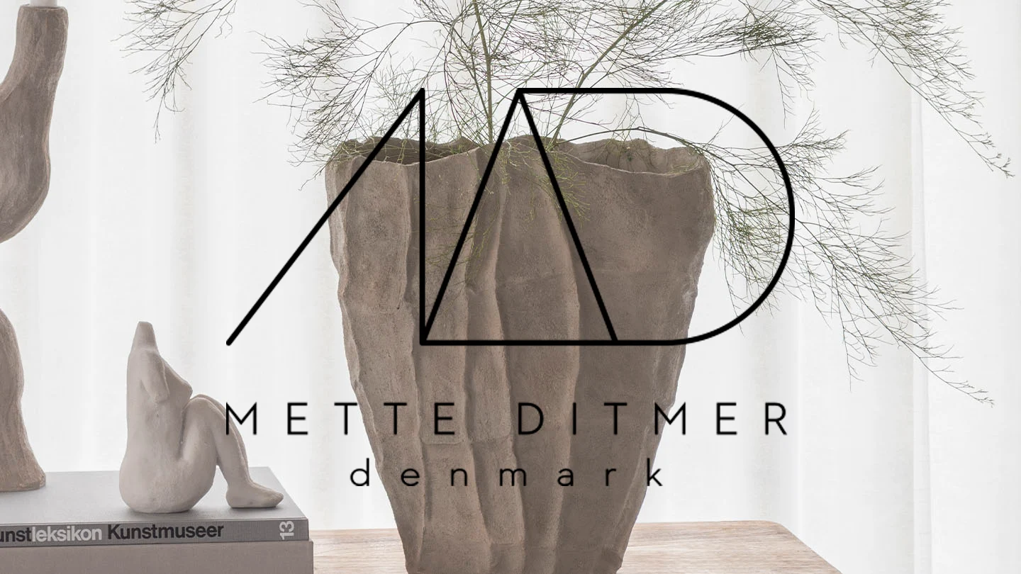 Stor, texturerad vas med gröna grenar, en sittande keramikfigur, och 'Mette Ditmer Denmark' logotyp.
